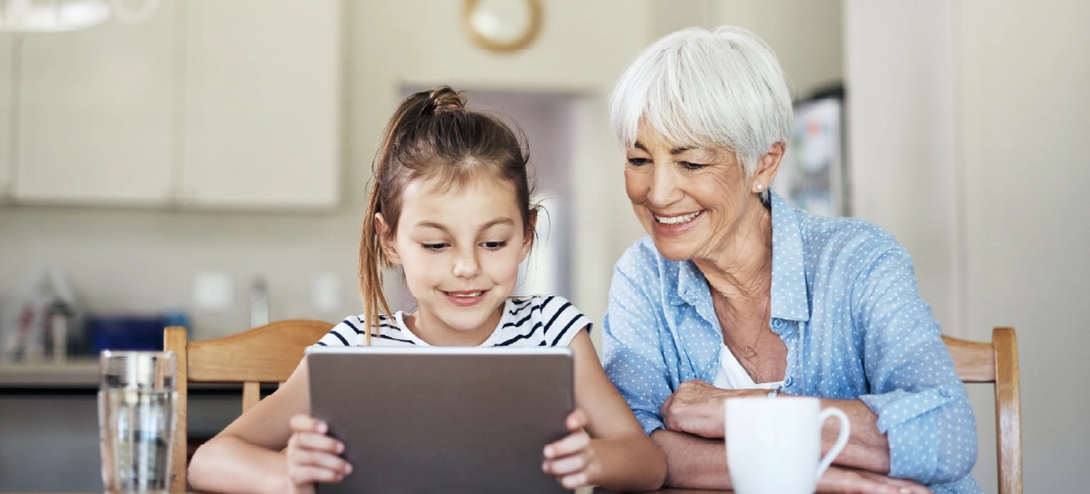 Grandparent and child smiling while using a tablet together