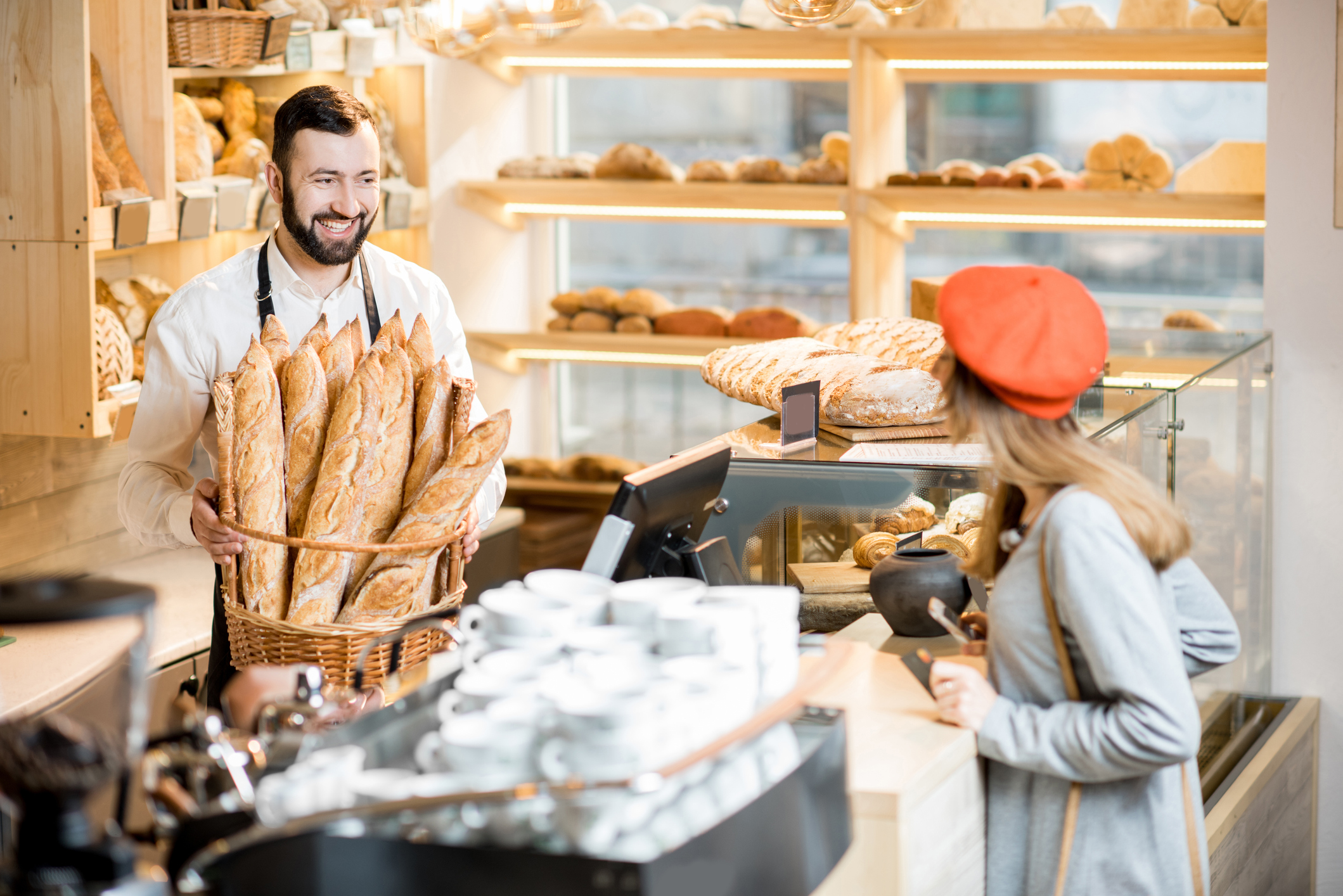 Bakery worker serving fresh baguettes to a customer in an artisan bakery.