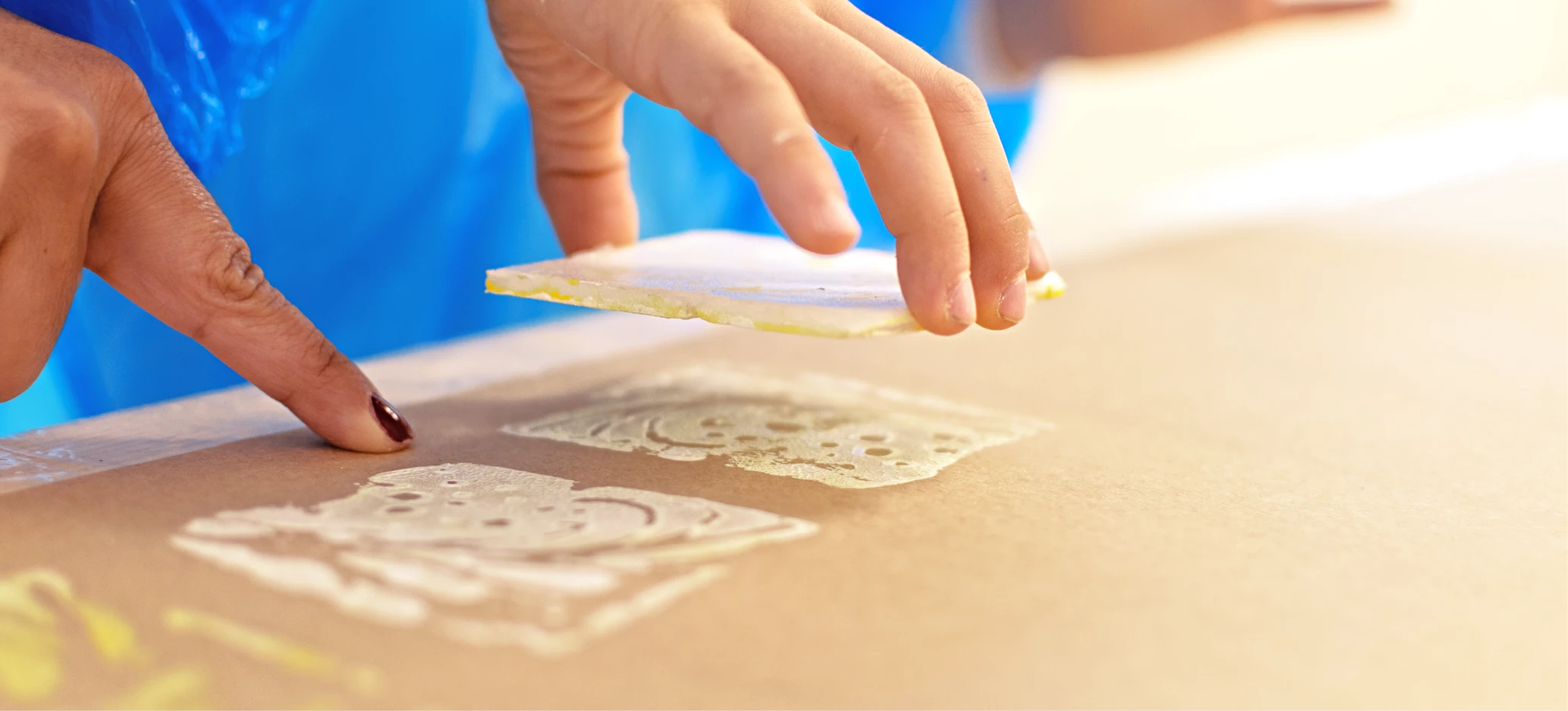 Close-up of a child’s hand using a decorated block to make a print on paper during an art activity.