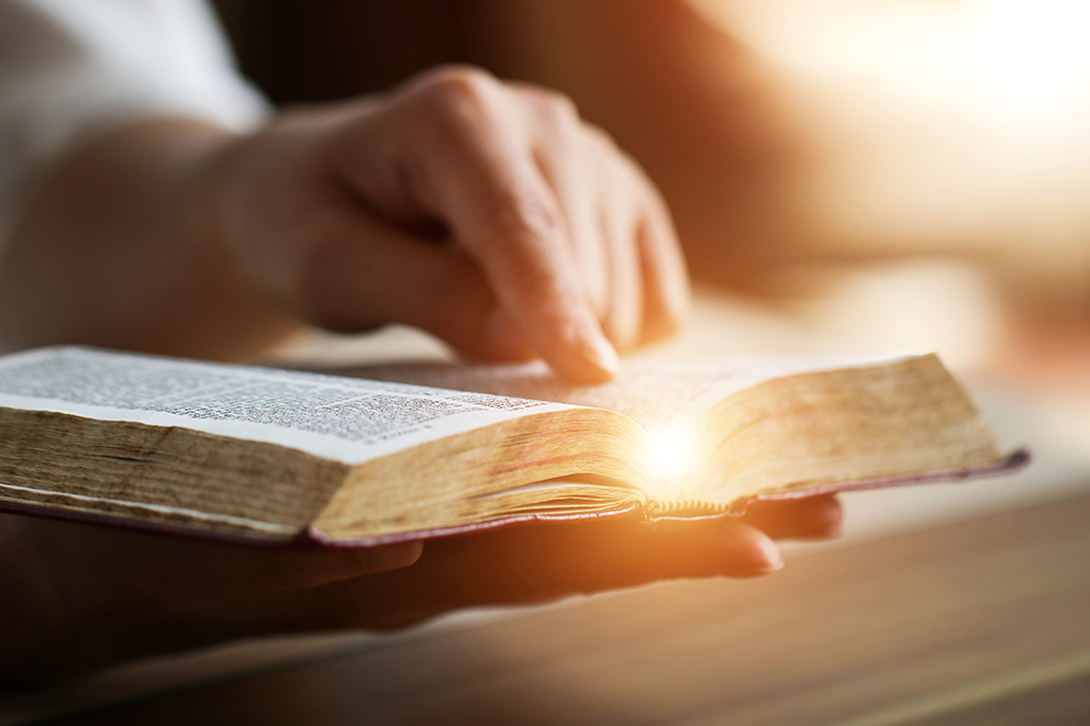 A hand pointing at a bible, with light shining from the centre.