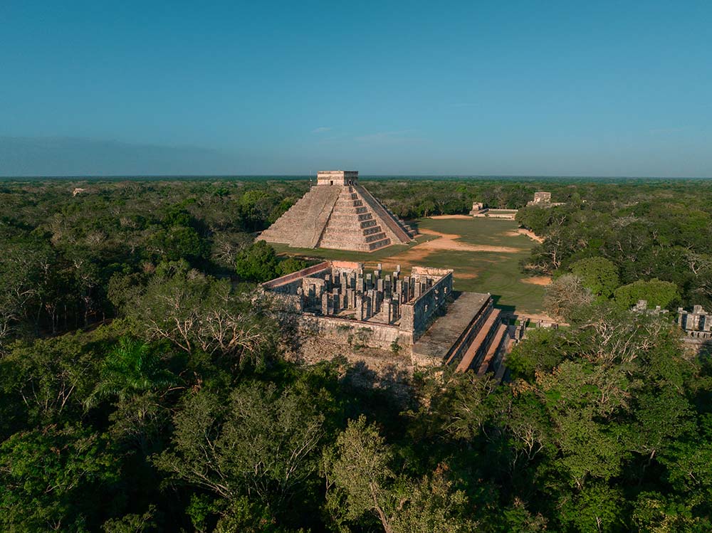 Large stone pyramid rising above a flat jungle landscape.