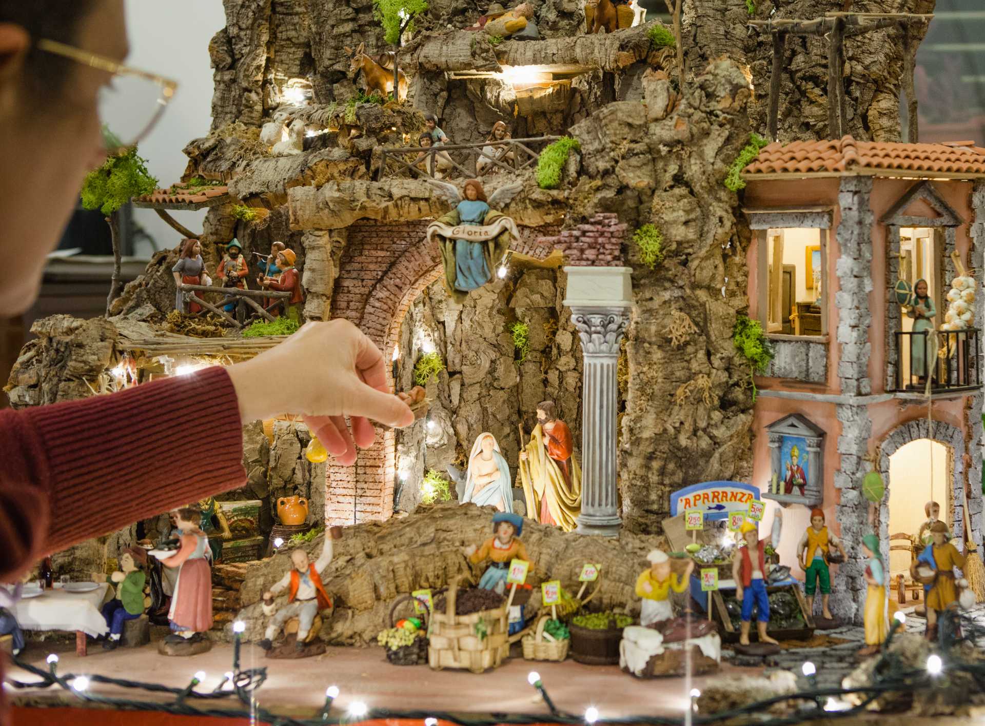A person is adding a figurine to a detailed model Nativity, with Mary and Joseph at the centre