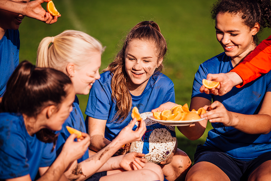 A group of girls in blue shirts sharing orange slices after a sports game, smiling and enjoying the moment.