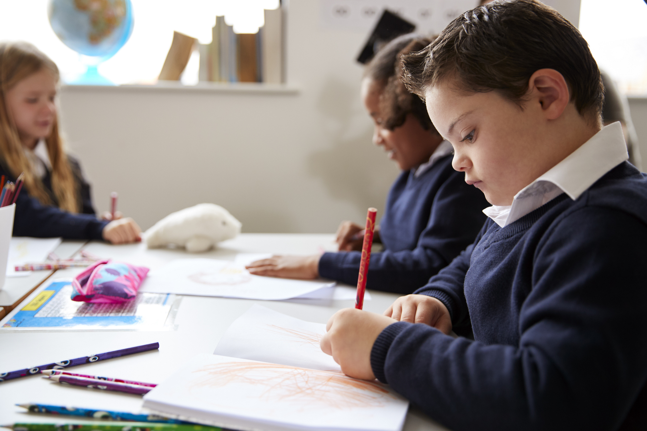 Children working and colouring at school, focusing on their artwork at a desk.