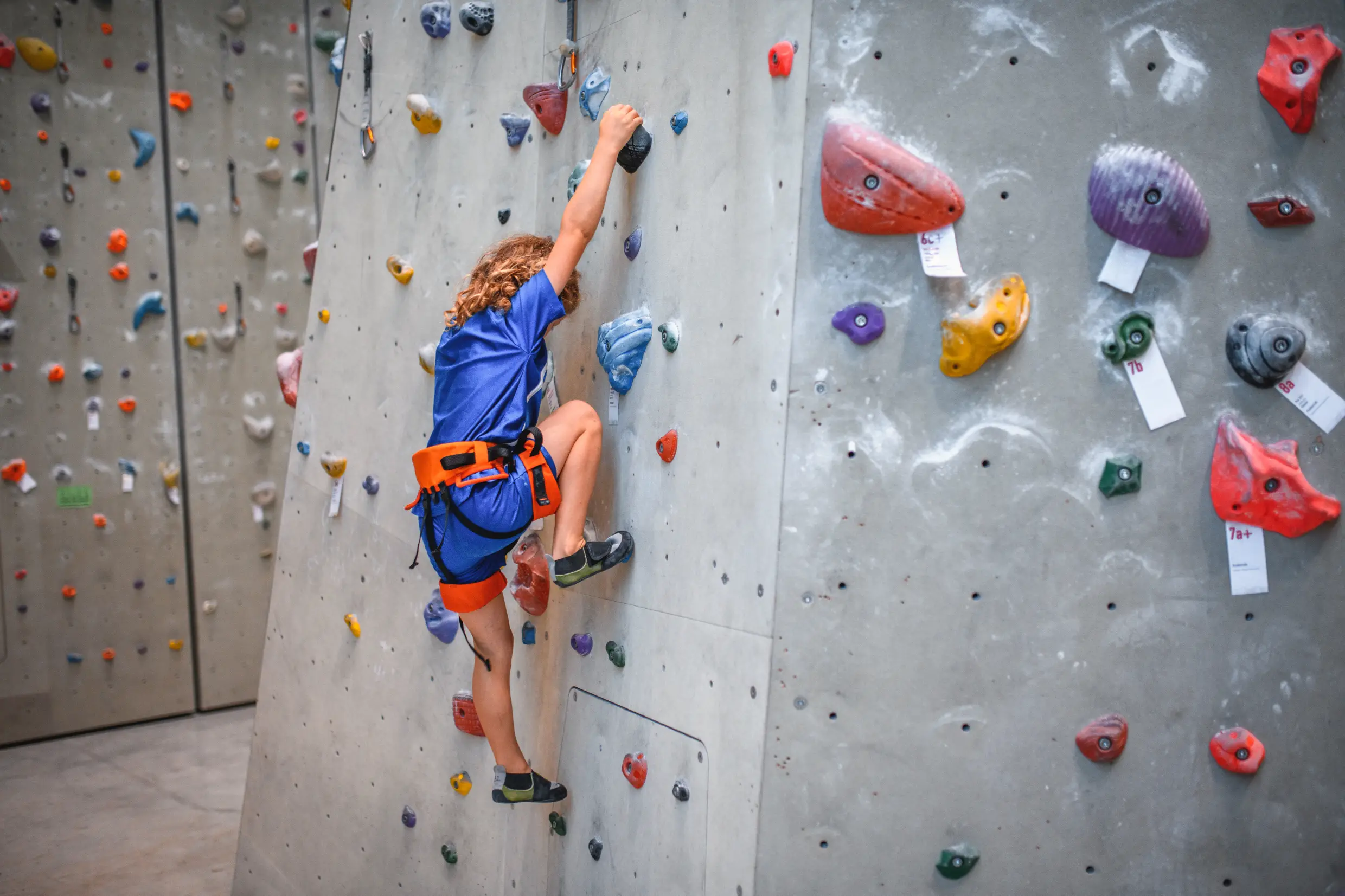 Child climbing an indoor wall with colourful holds.