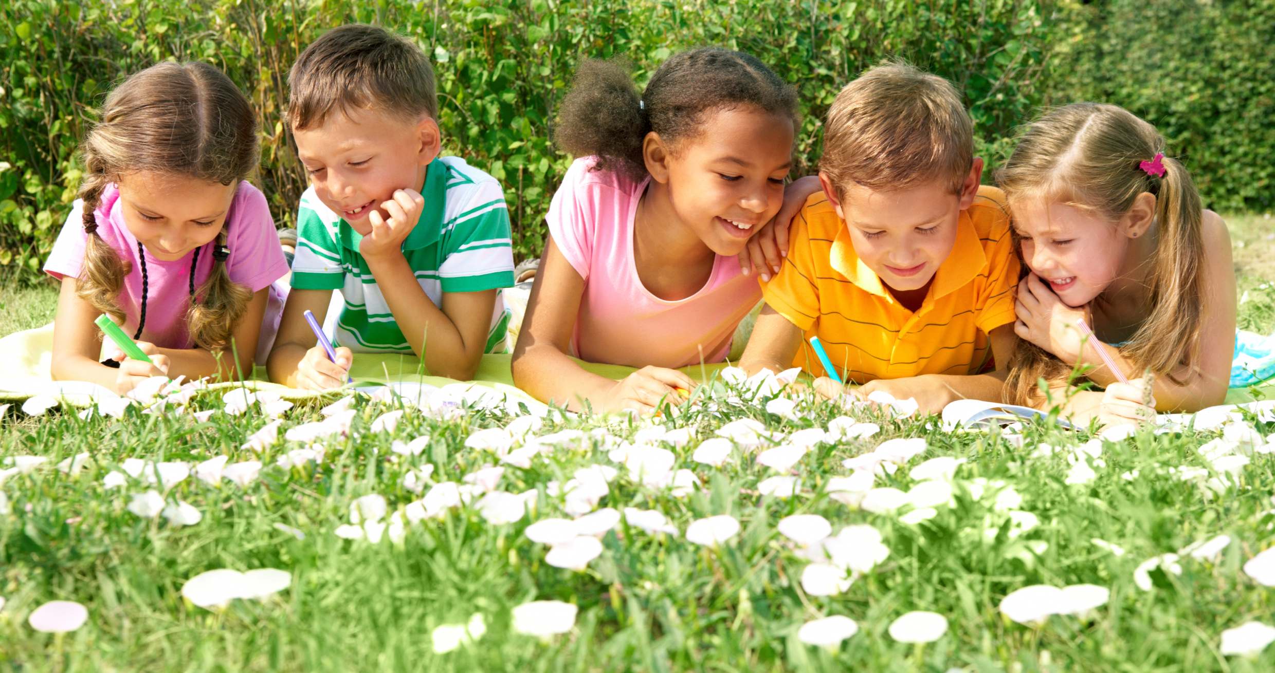Children lying on the grass writing and smiling together