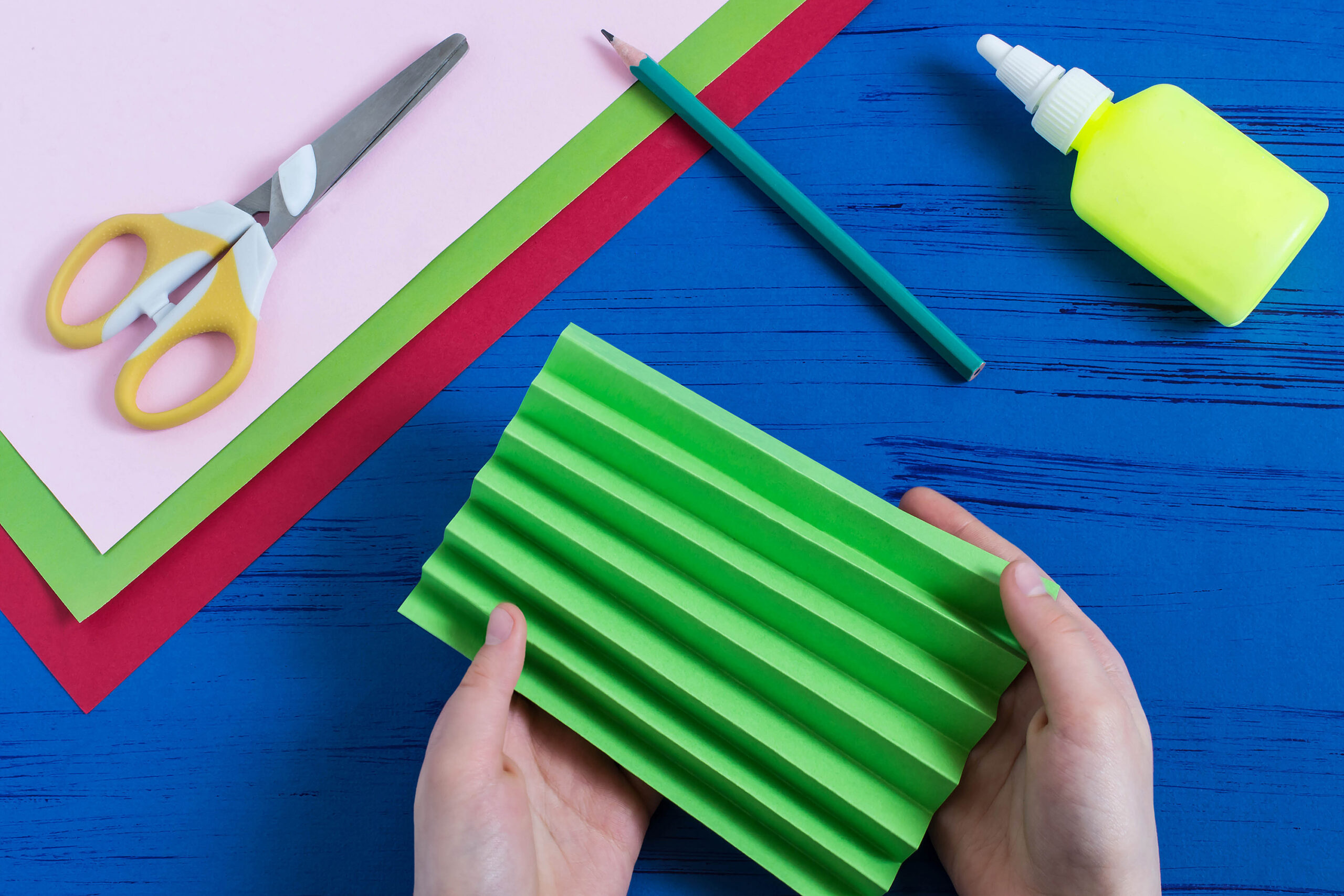 Hands holding folded green paper with craft tools on a table.