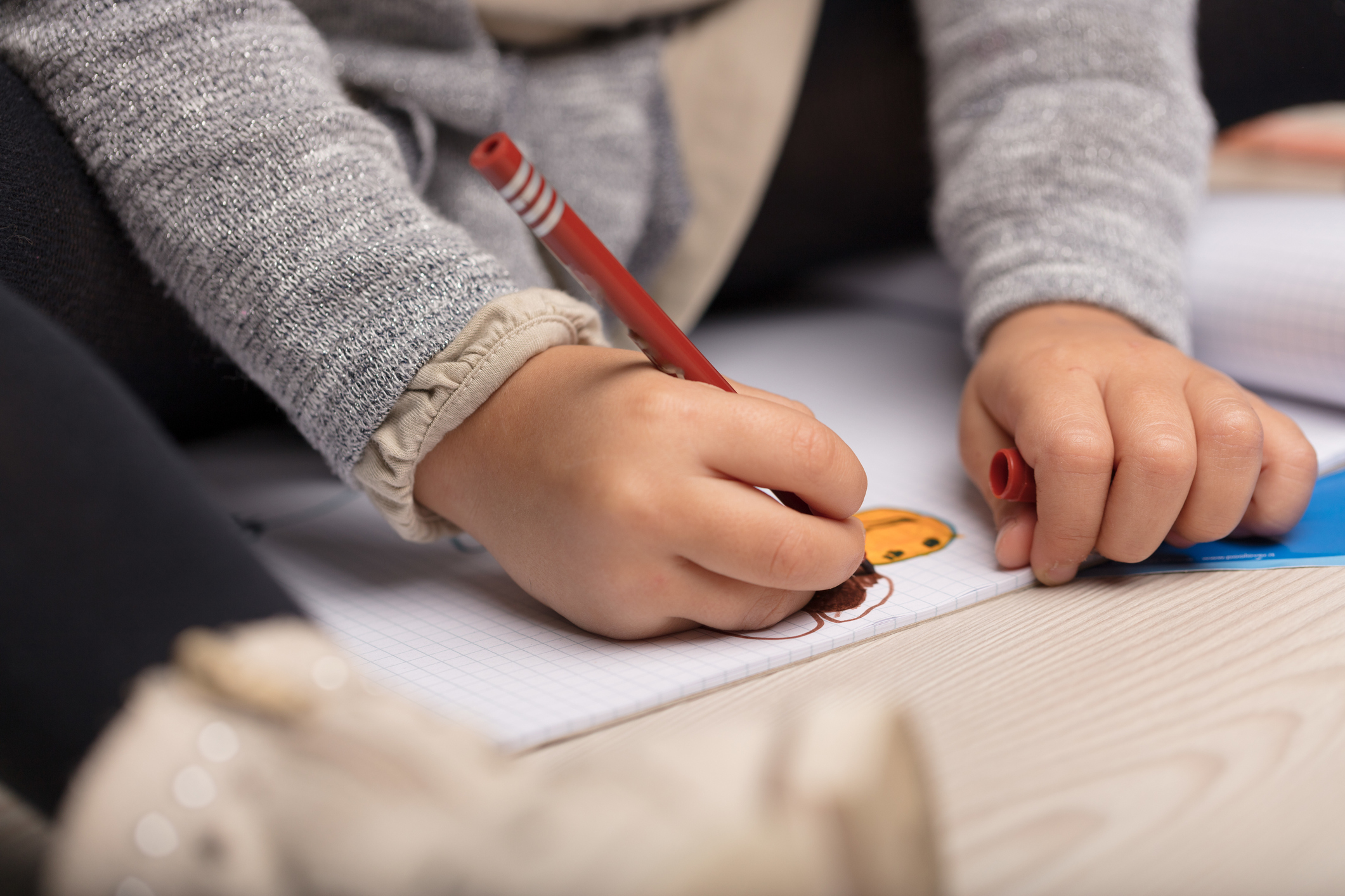 Close-up of child’s hands drawing and colouring on squared paper with red and orange felt-tip pens.