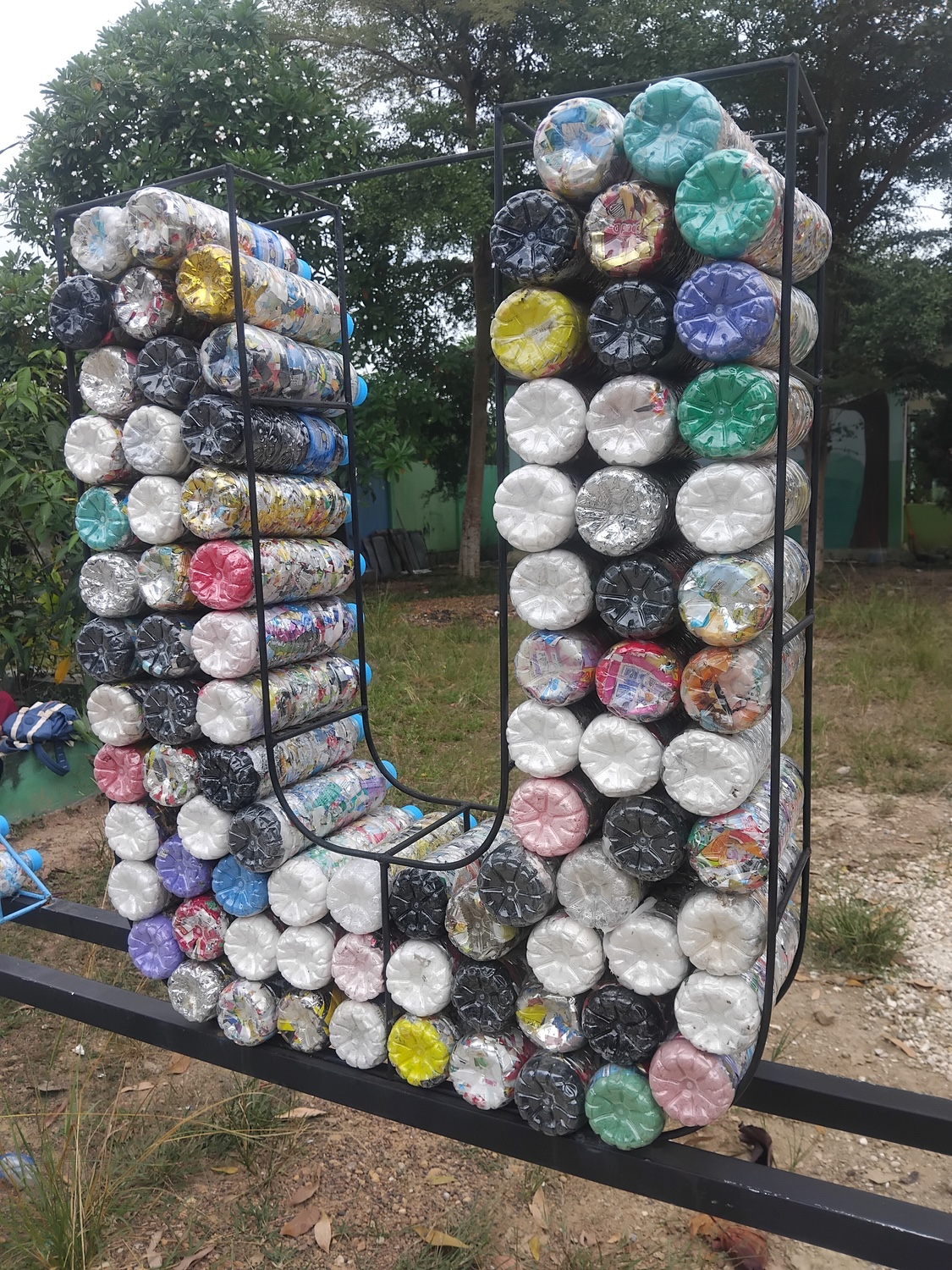 U-shaped structure made from tightly packed plastic bottles held in a metal frame outdoors.