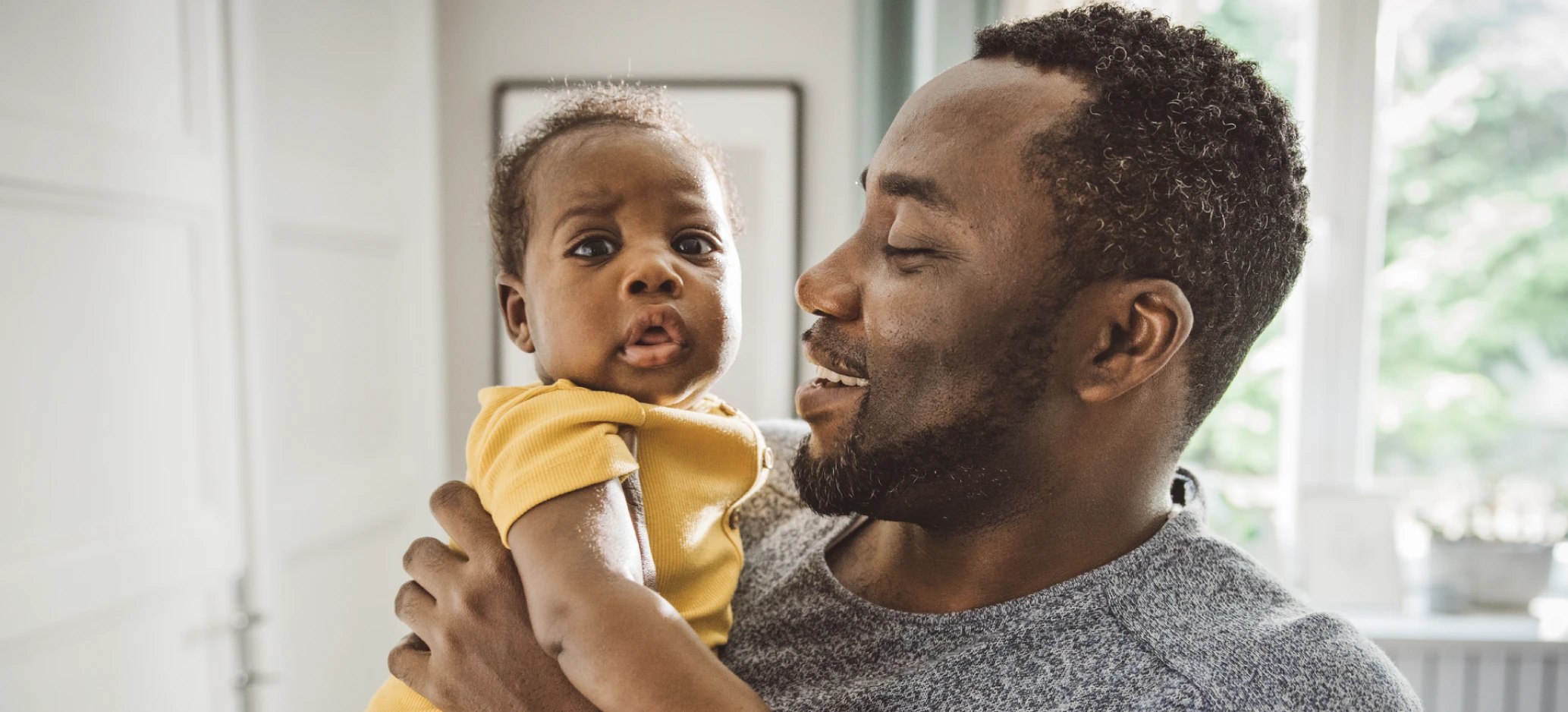 Father holding his baby and smiling at home.