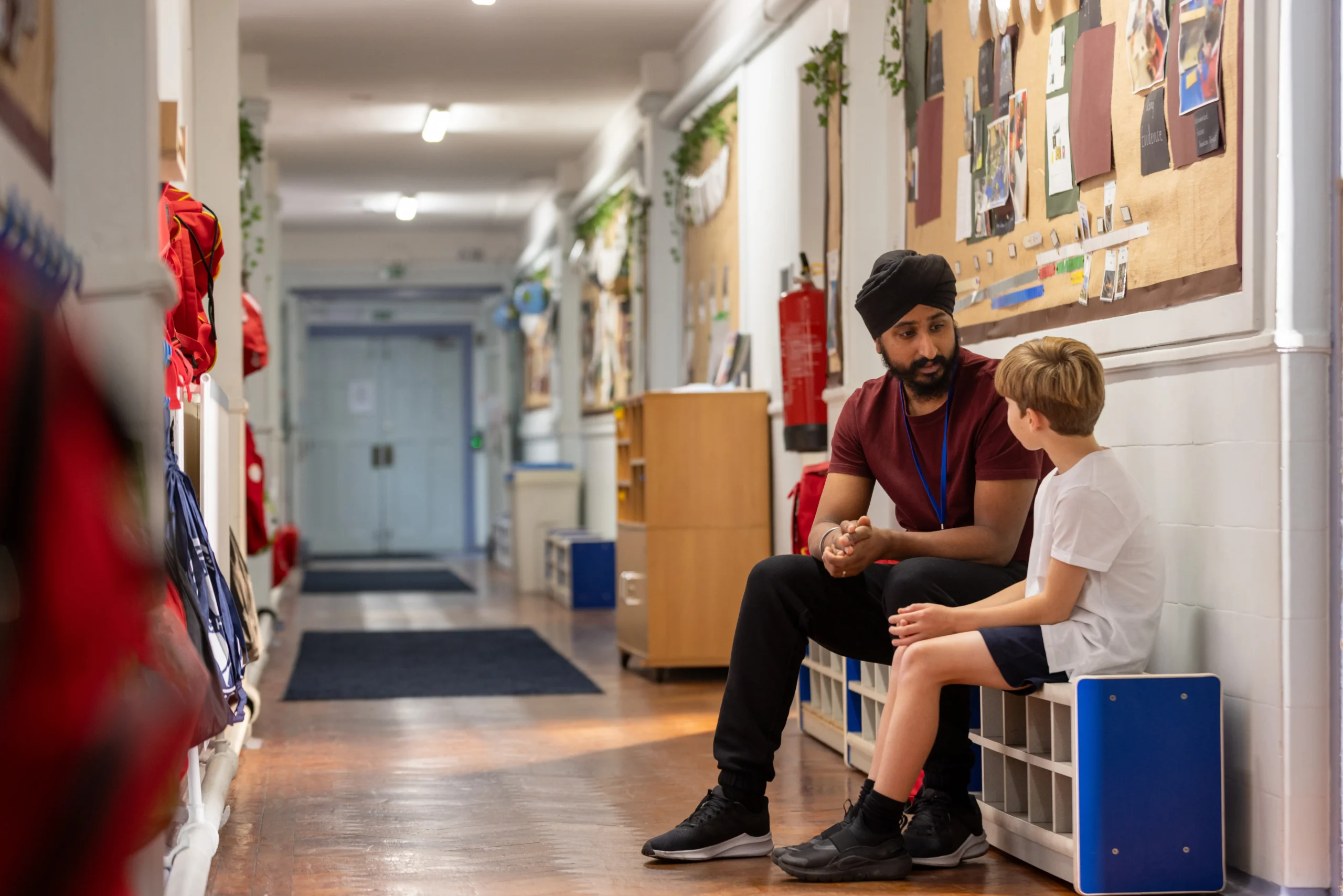 School staff member talking with a pupil seated in a school corridor