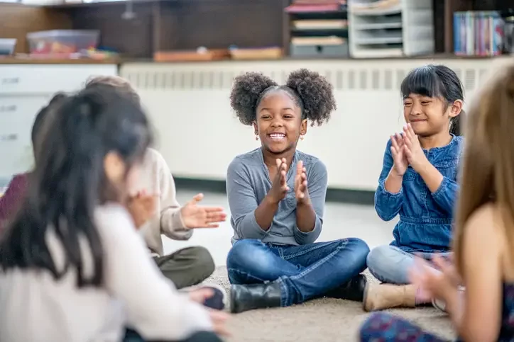 Children sitting on the floor in a circle, clapping together during a group activity.