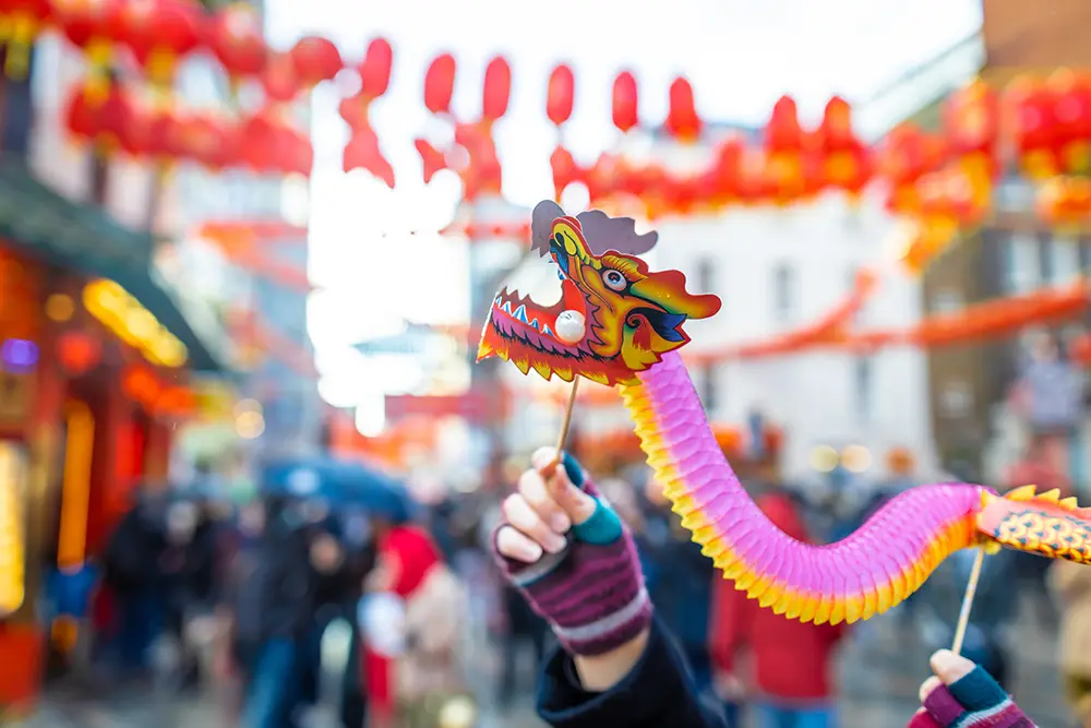 Hands hold a dragon puppet against a blurred, busy street celebrating lunar new year