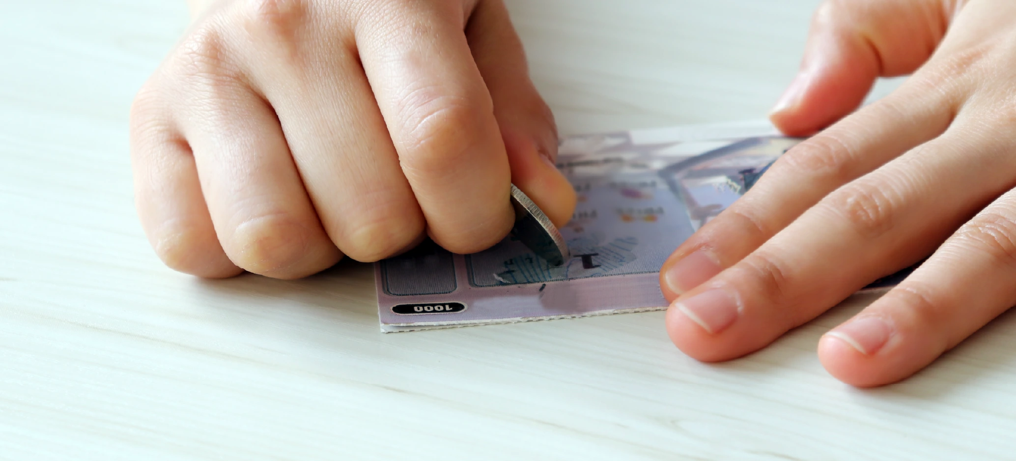 A person scratching a scratch card with a coin.
