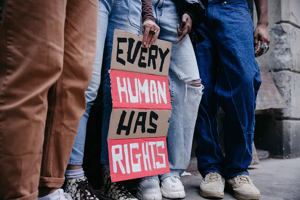 A person among a group holds a cardboard sign reading “Every human has rights”.