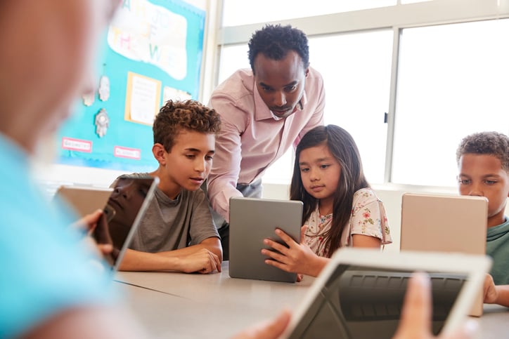 teacher showing primary school pupils how to work tablet device