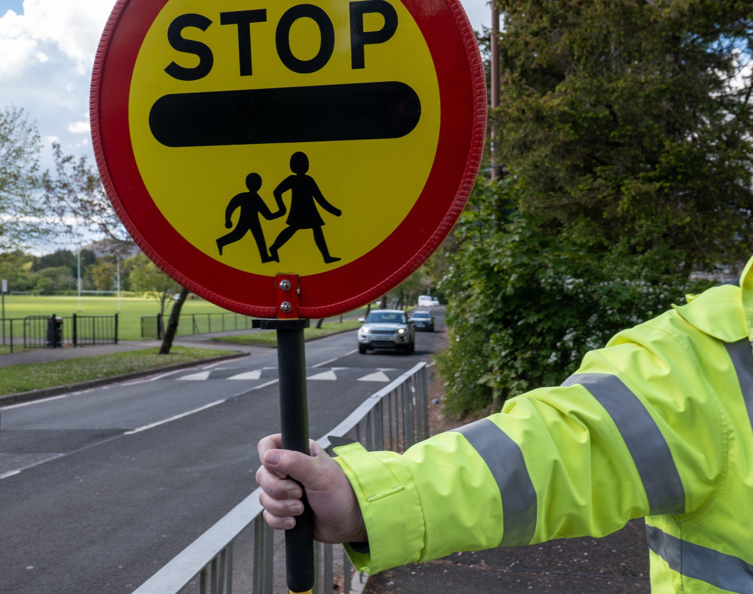 A school lollipop crossing sign held by lollipop person