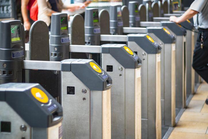 A row of ticket barriers at a train or underground station, each with a contactless payment reader.