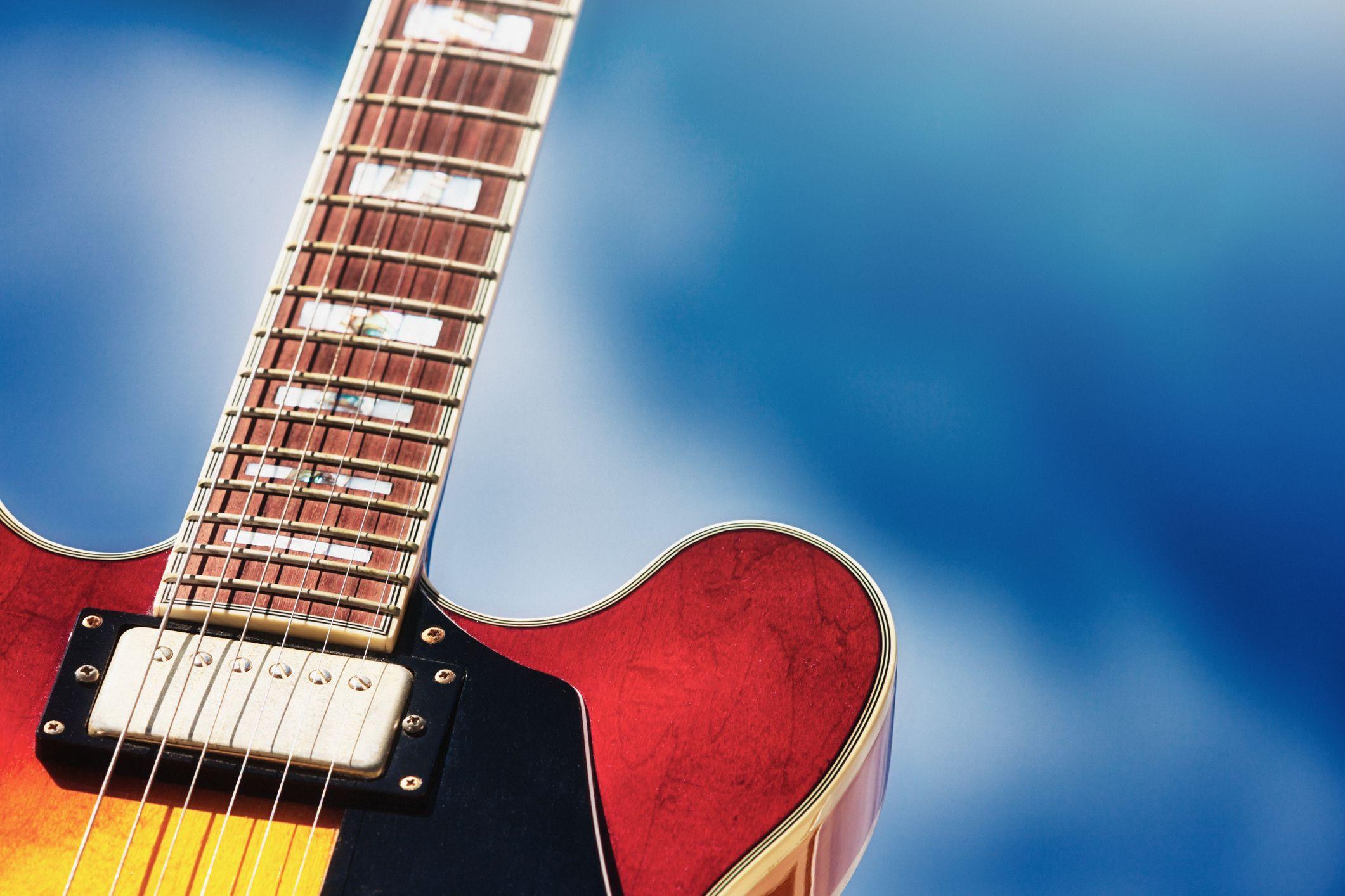 Close-up of a red electric guitar neck and body against a blue background.
