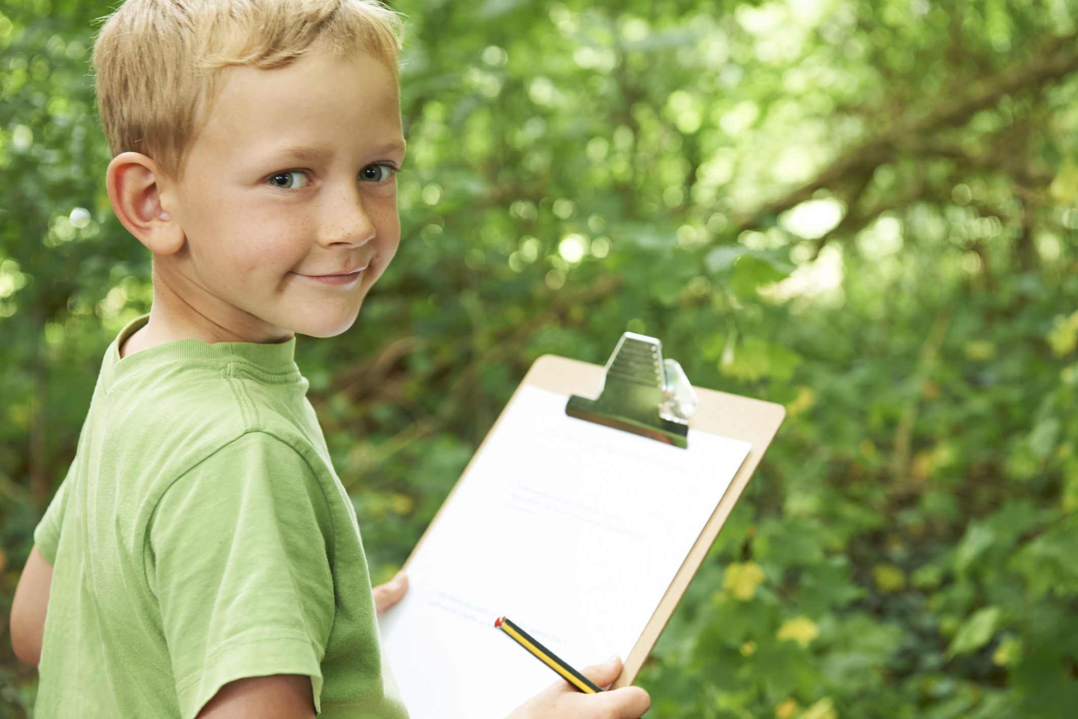 A young boy outside holding a pencil and a clipboard.