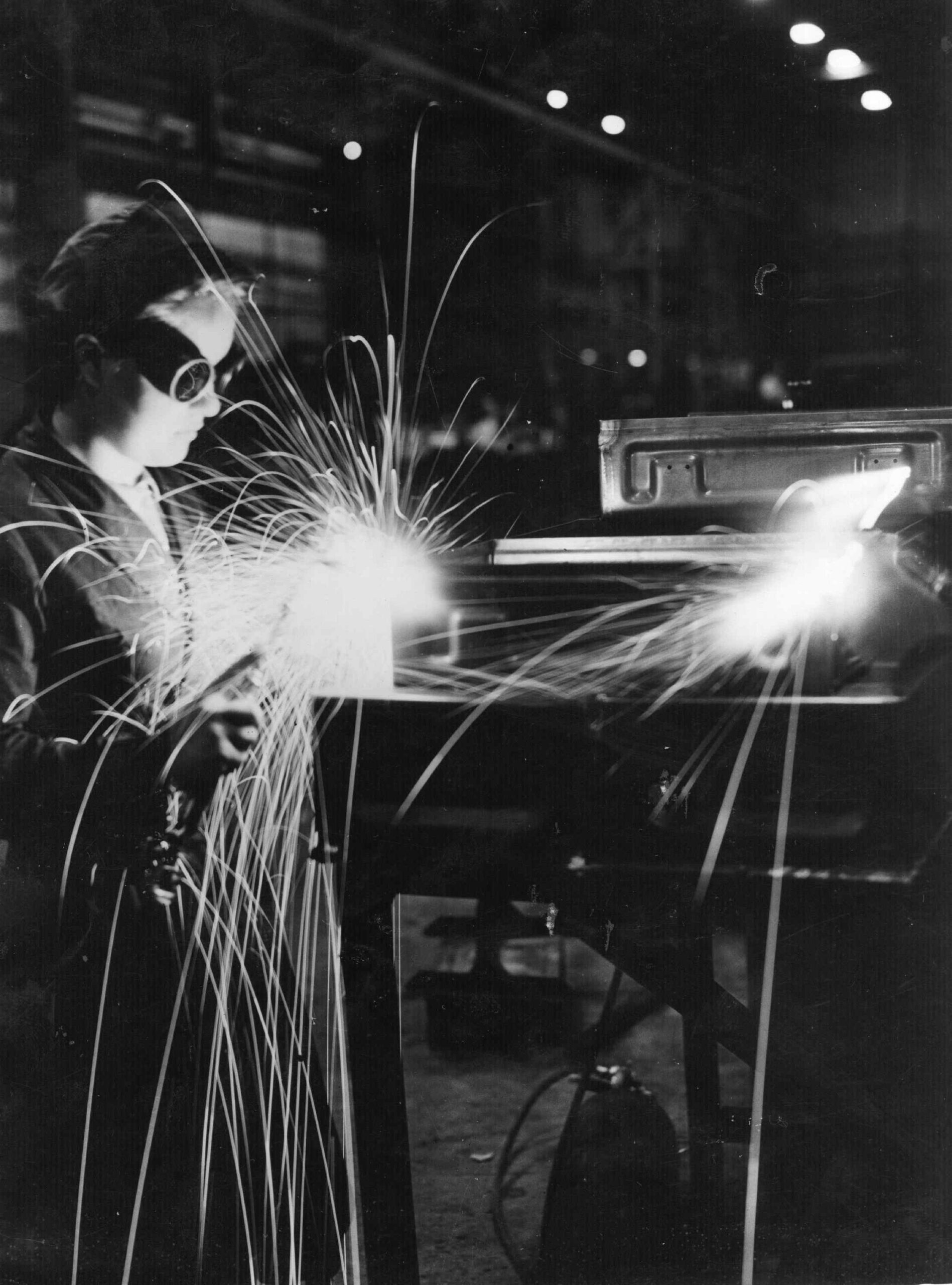 Female engineer wearing goggles welding metal, surrounded by sparks, during World War II.