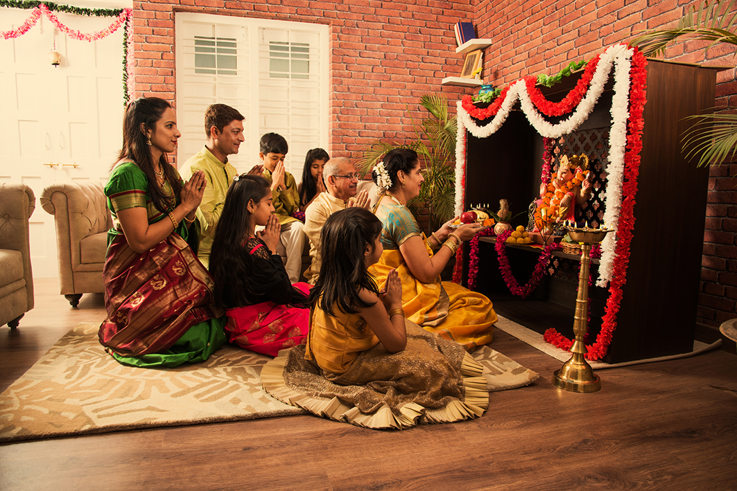 Family performing prayer ritual with offerings in front of a Ganesha idol during a festive occasion.