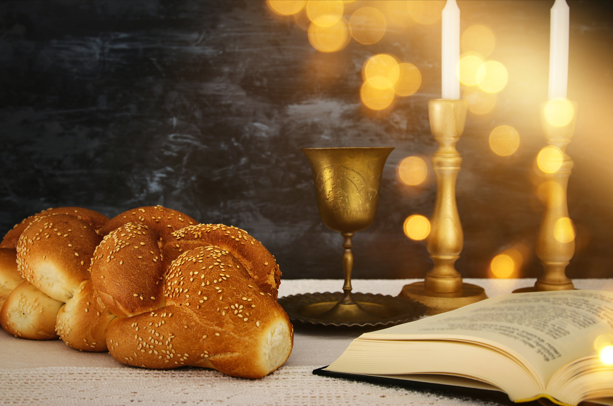 Challah bread, a wine cup, candlesticks, and an open book set for Shabbat.