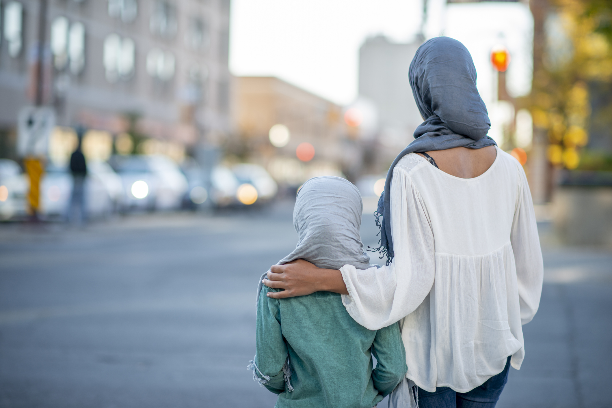A woman and child wearing hijabs walk together in a city street.