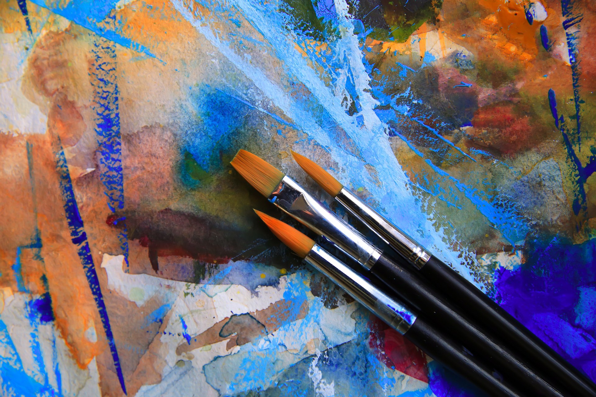 Three paintbrushes on a vibrant watercolour painting background.