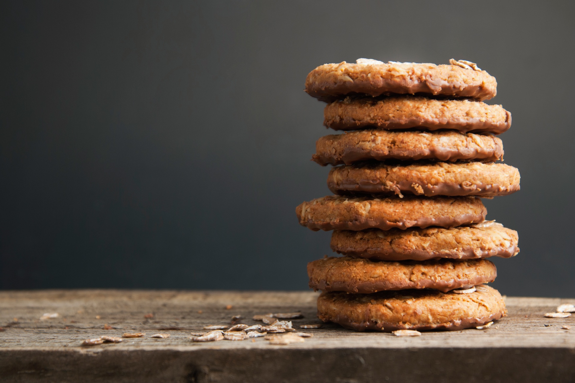 A stack of seven oatmeal cookies on a rustic wooden surface with a dark background.