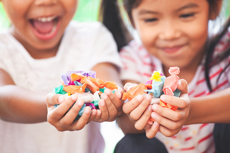 Two children hold colourful wrapped sweets in their hands.