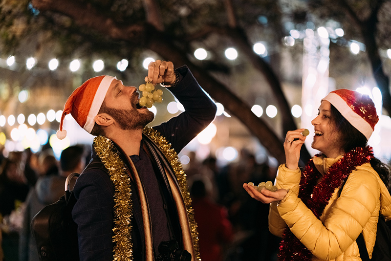Couple in Santa hats eating grapes during festive celebration outdoors