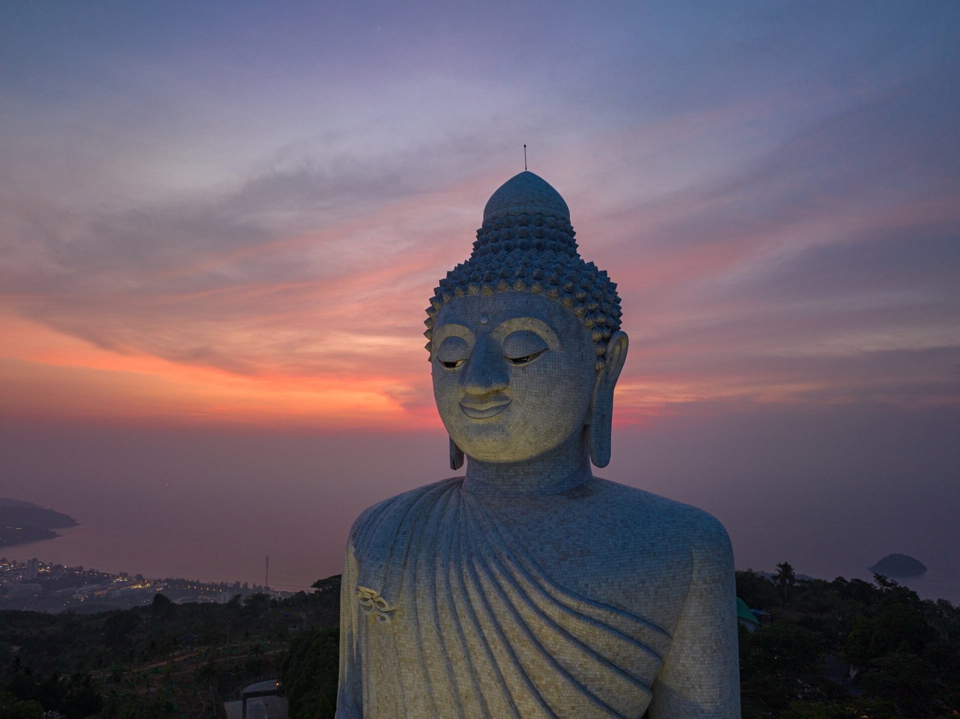 Giant Buddha statue overlooking coastal town at sunset