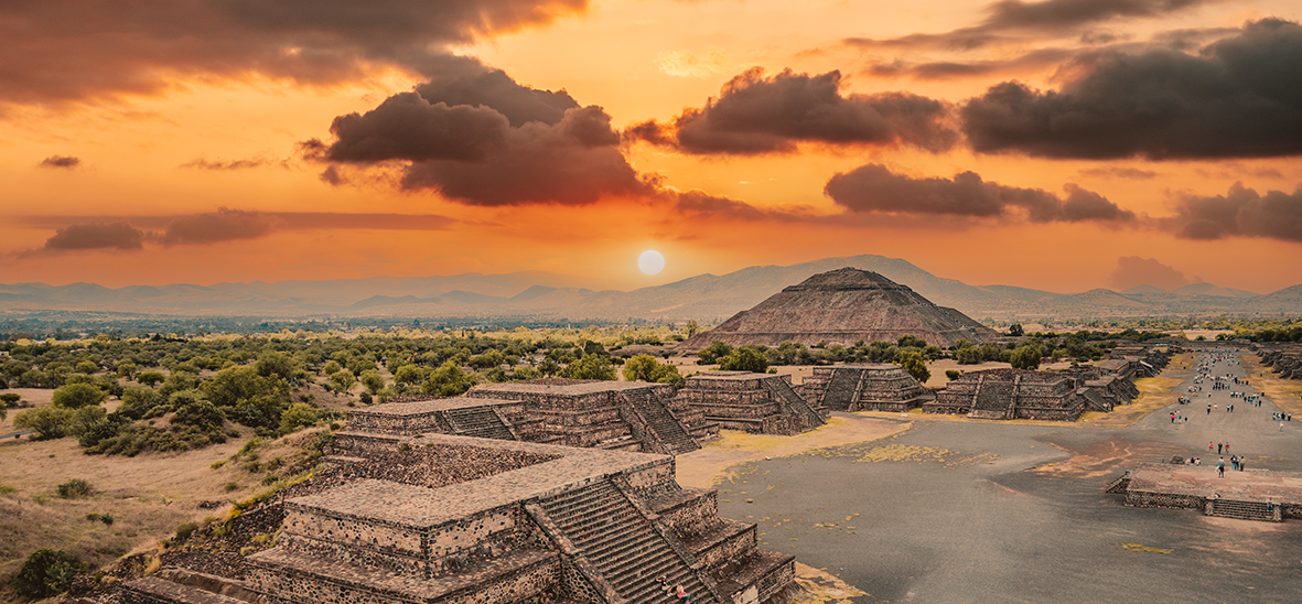 An ancient Mayan city with a mountainous landscape and sunset in the background