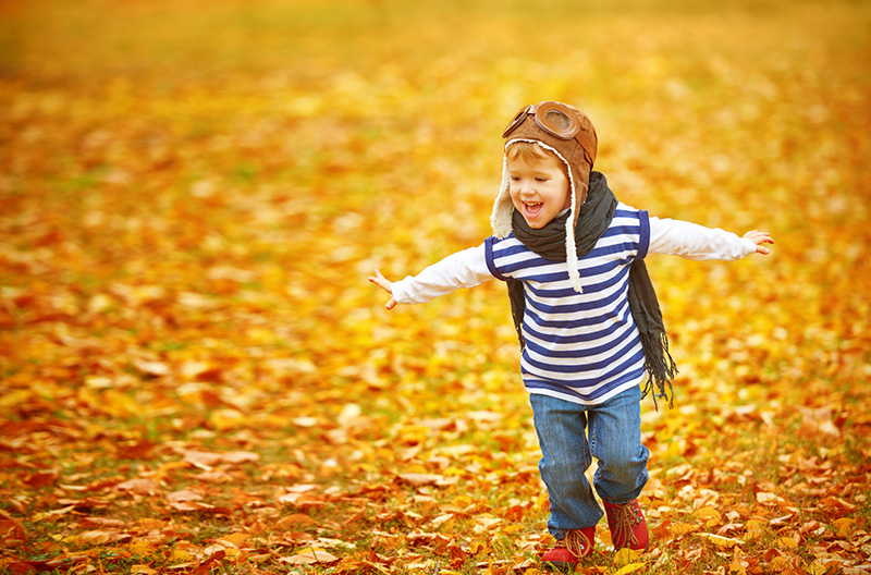 A young child running through fallen autumn leaves with arms outstretched.