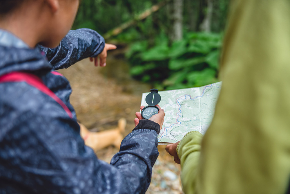 Two people using a map and compass while walking in a forest.