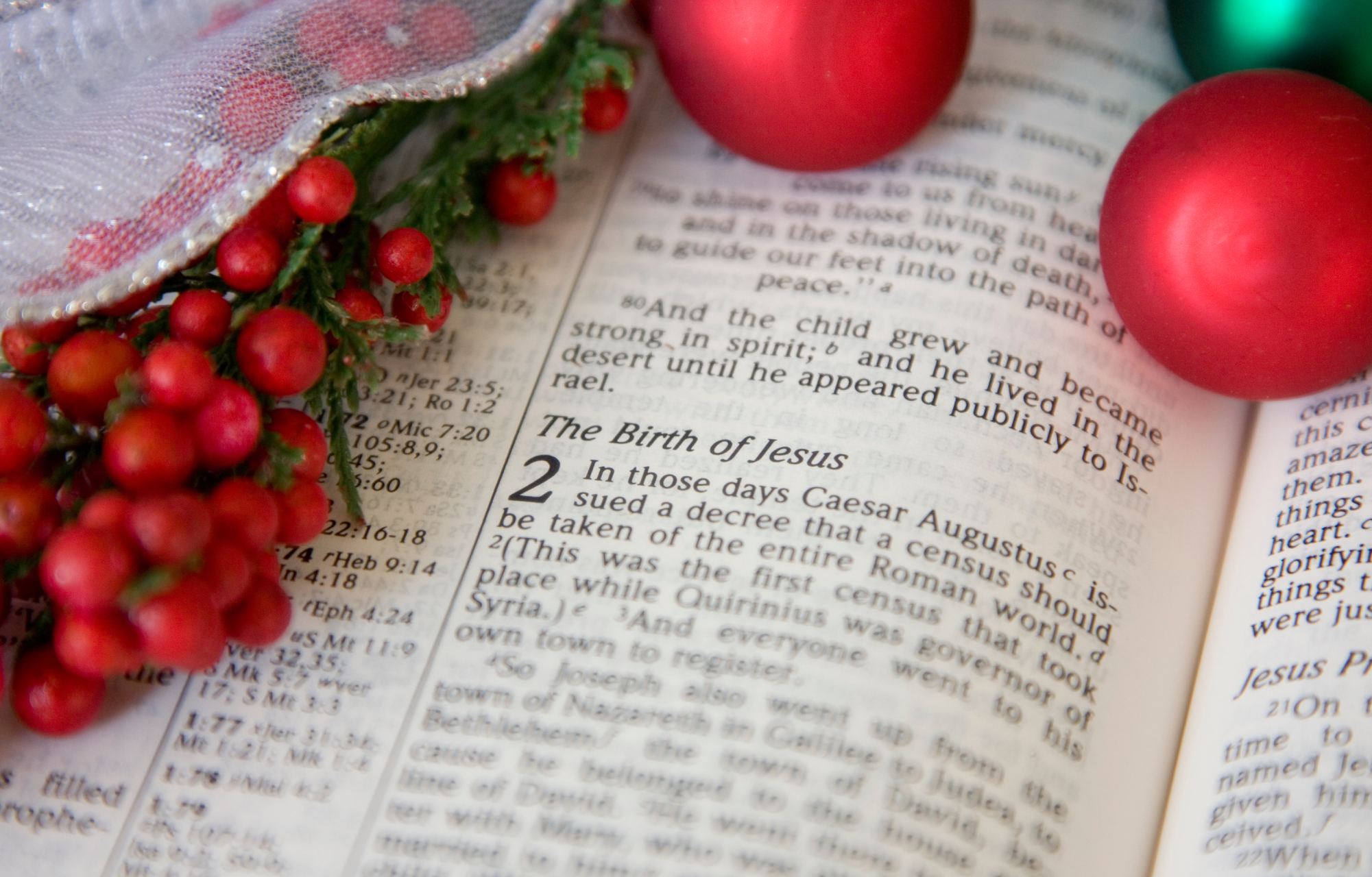 A Bible open to a passage about the birth of Jesus, with red Christmas decorations laid out on the pages