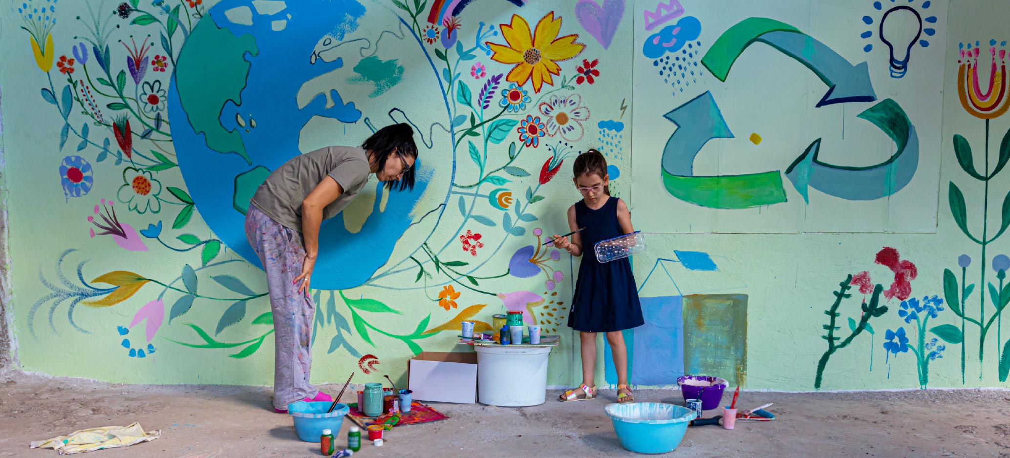 child and adult painting a mural on a wall