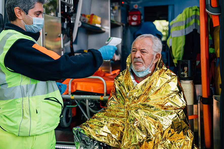 Paramedic checking elderly man’s temperature in an ambulance after an emergency.