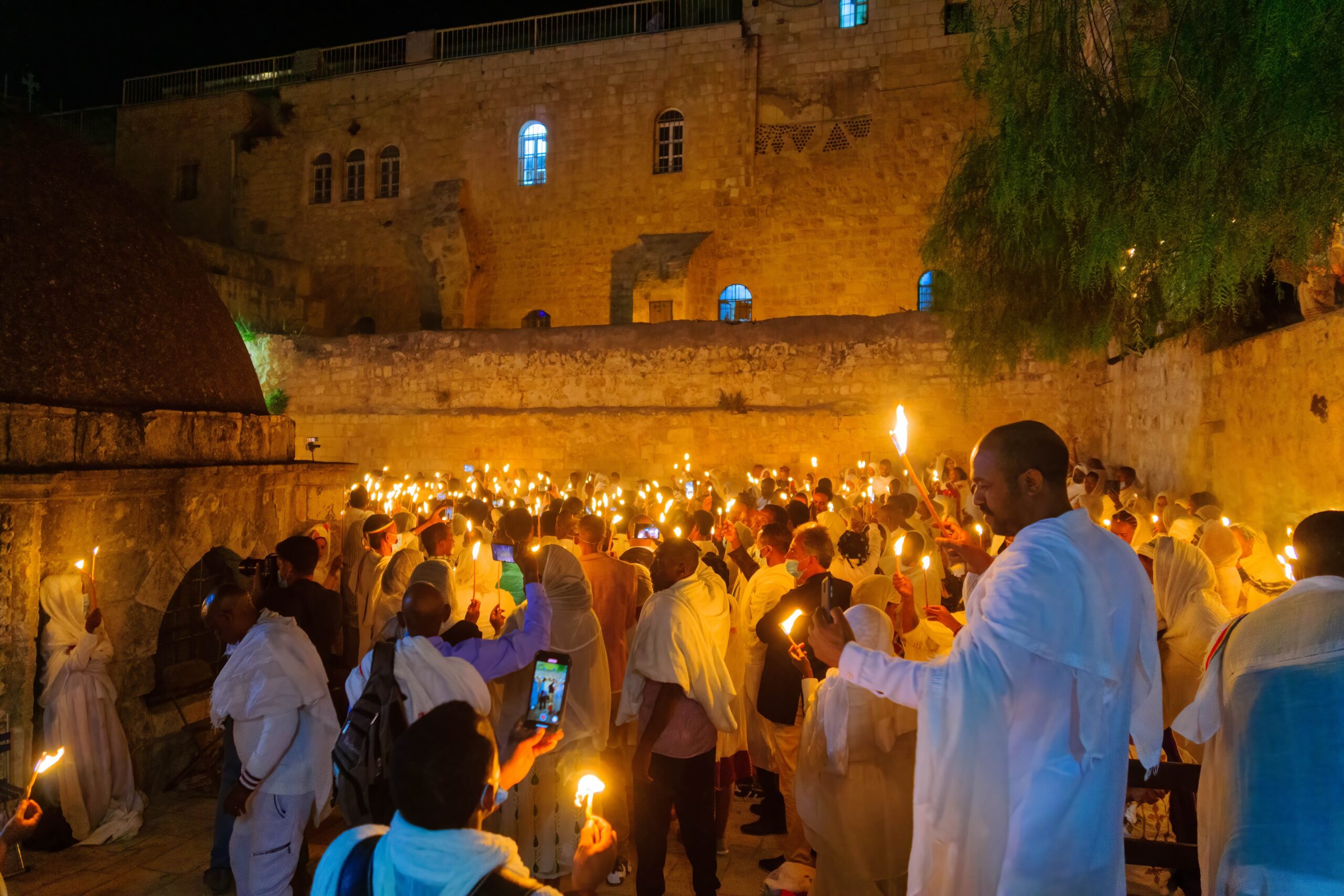 Nighttime candlelight gathering at the Western Wall with attendees in traditional attire.