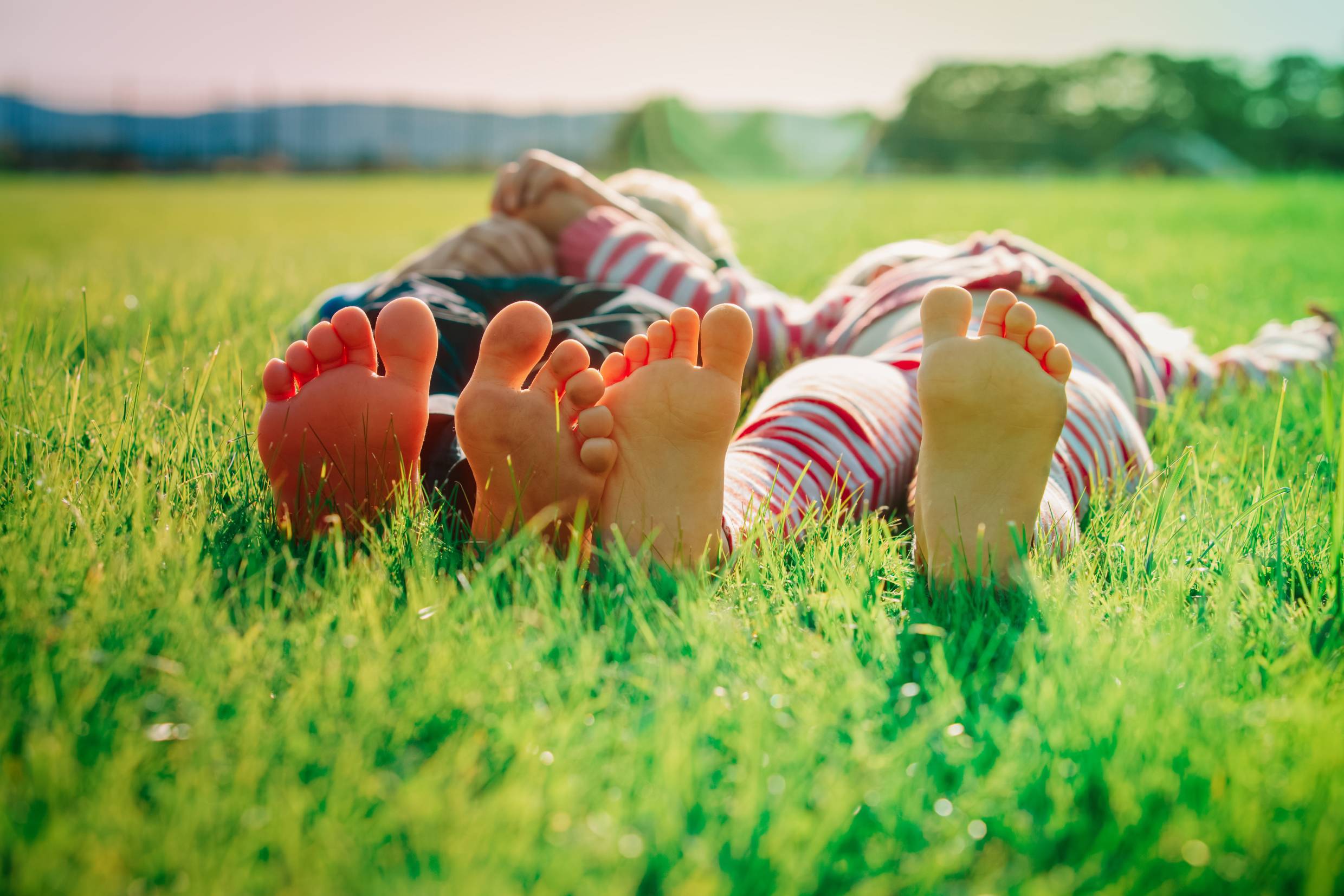 Bare feet of two children lying on their backs in the grass on a sunny day.
