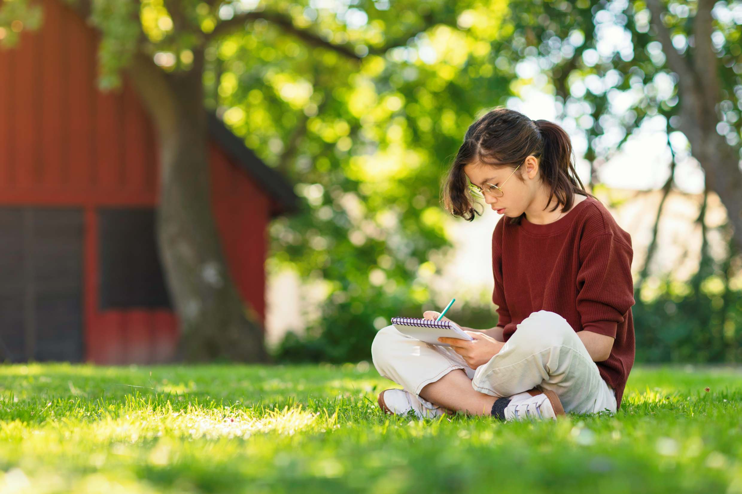 A girl reading or journaling outside in a natural setting.