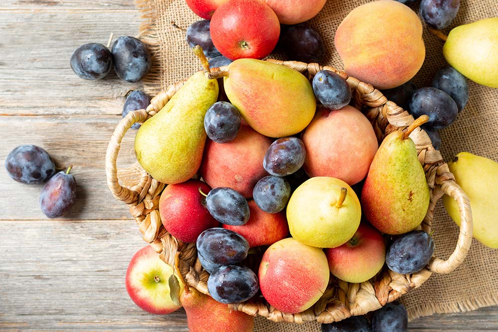 Basket of pears, apples, peaches, and plums on a wooden surface.