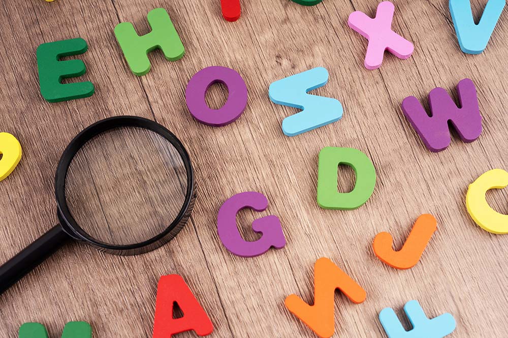 Colourful alphabet letters with a magnifying glass on wooden background.
