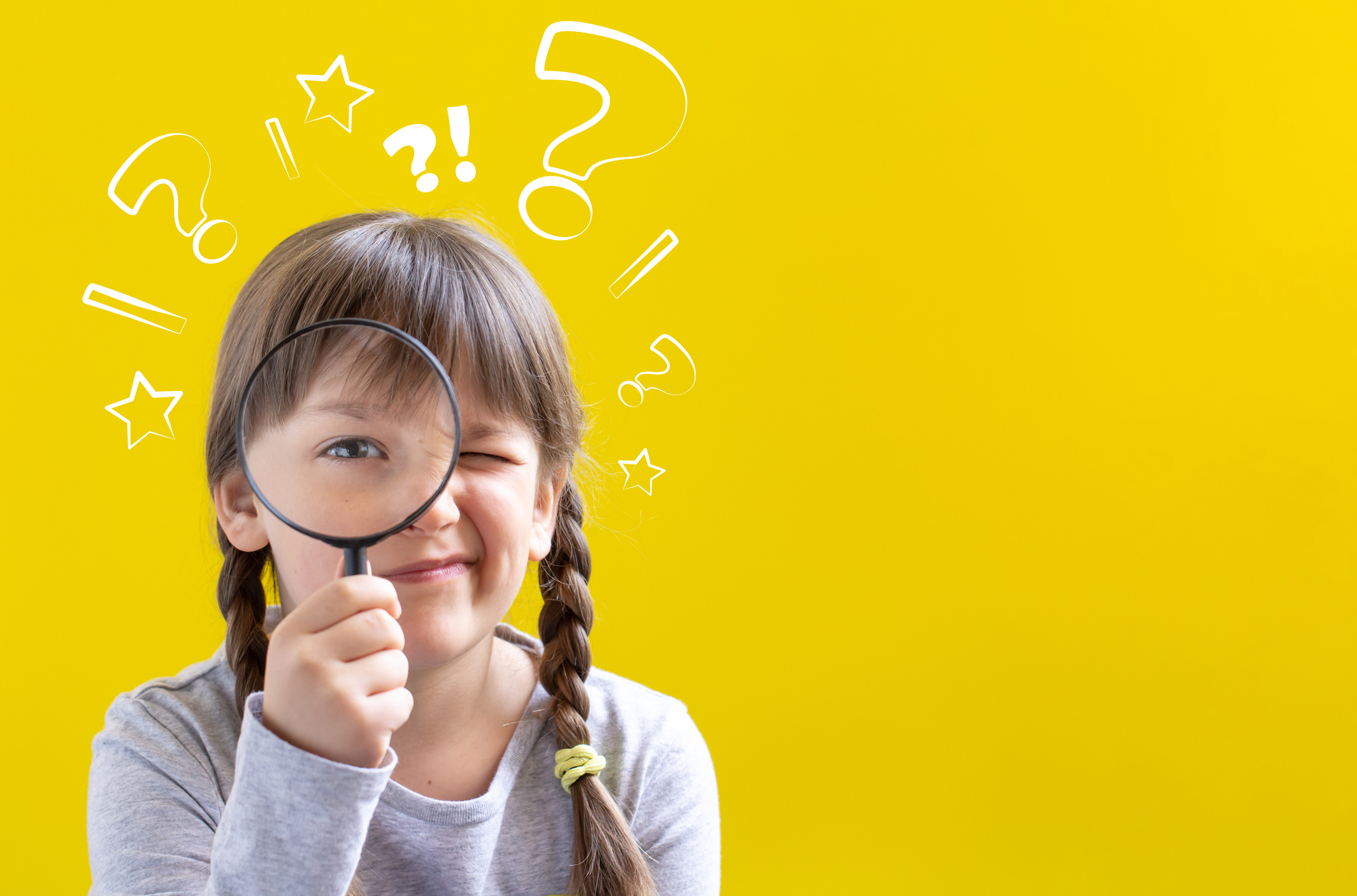 Child holding a magnifying glass against a yellow background.