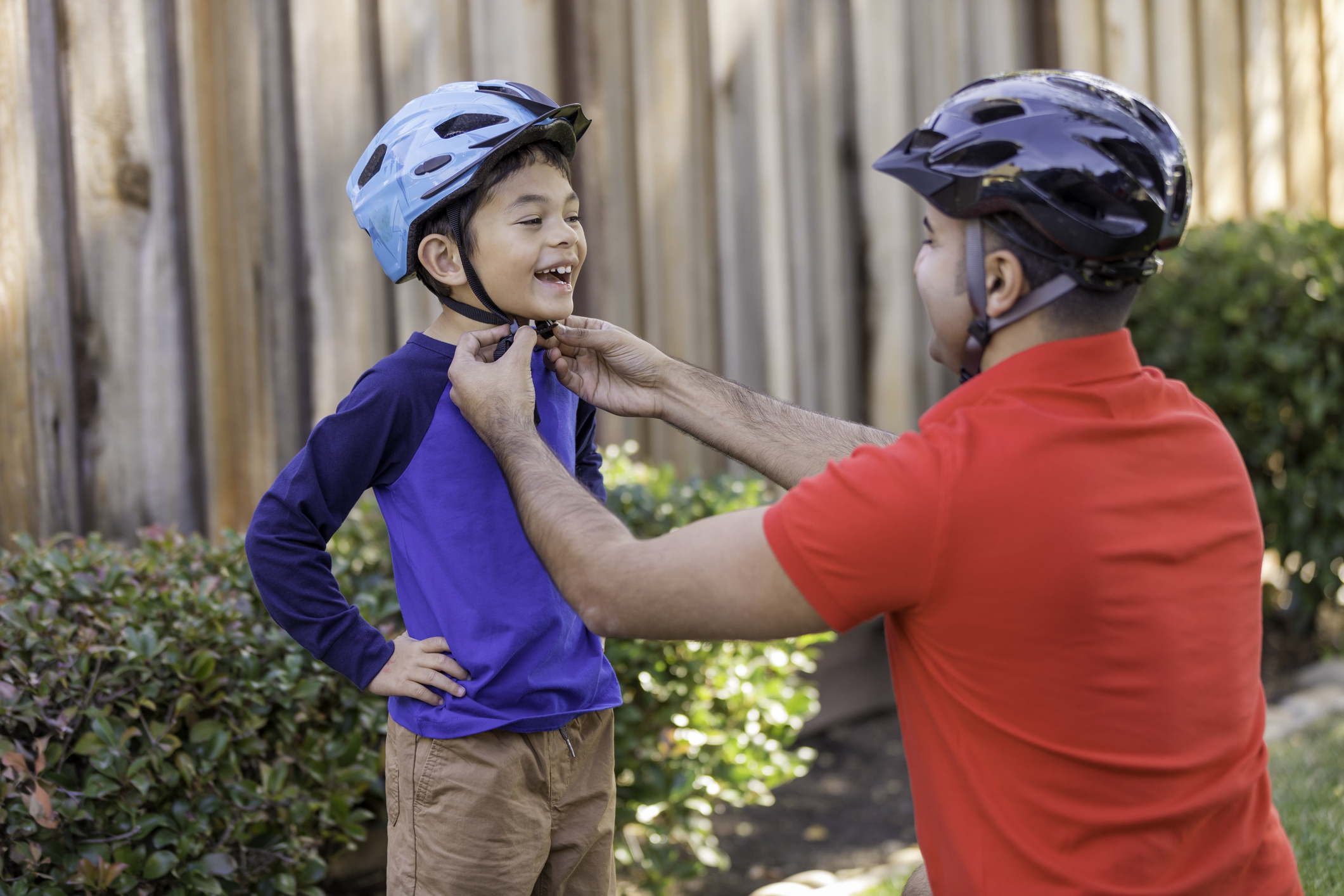 An adult adjusts a child’s bicycle helmet strap.