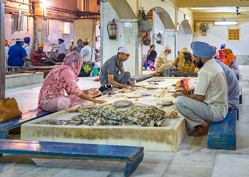 People sitting on low platforms preparing food together in a large communal kitchen.