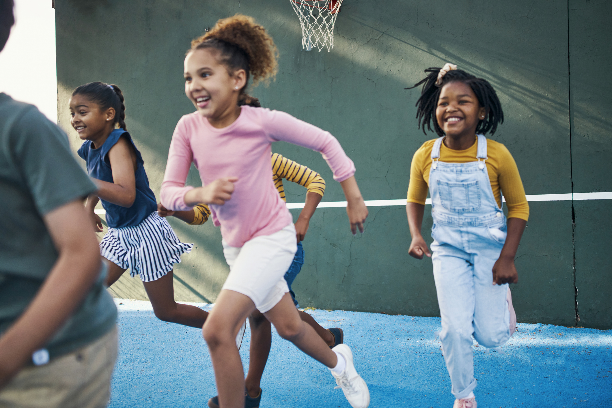 Children running and playing on a playground court, smiling and enjoying outdoor activity.