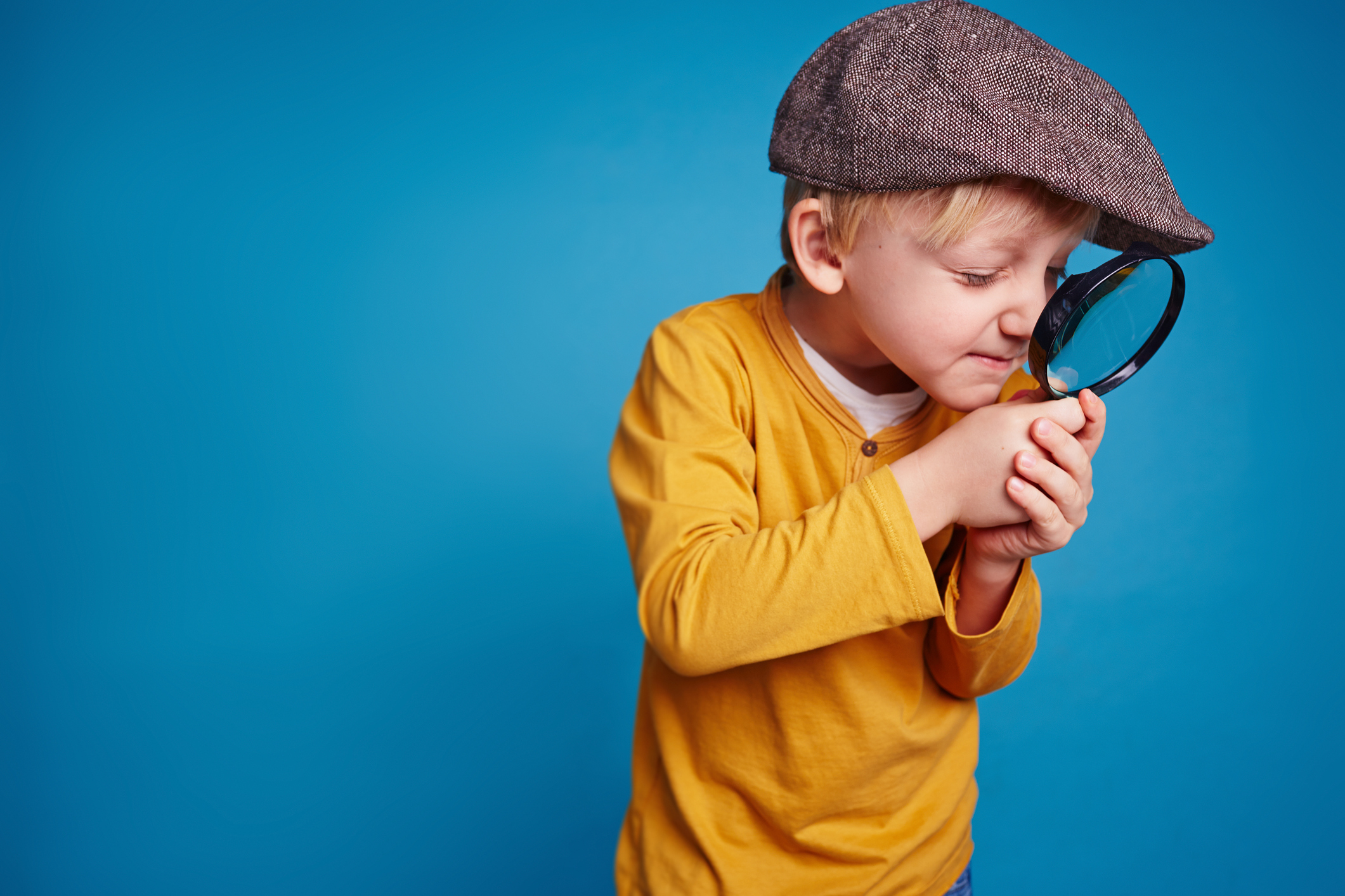 Boy in yellow shirt using magnifying glass against blue background.