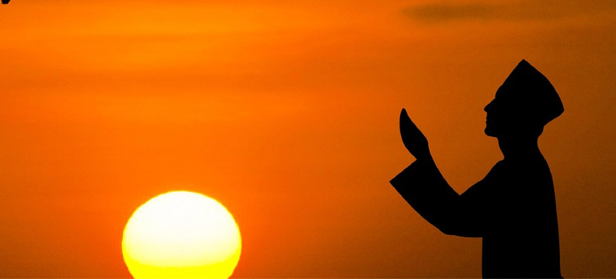 Silhouette of a person praying at sunset with hands raised against an orange sky.